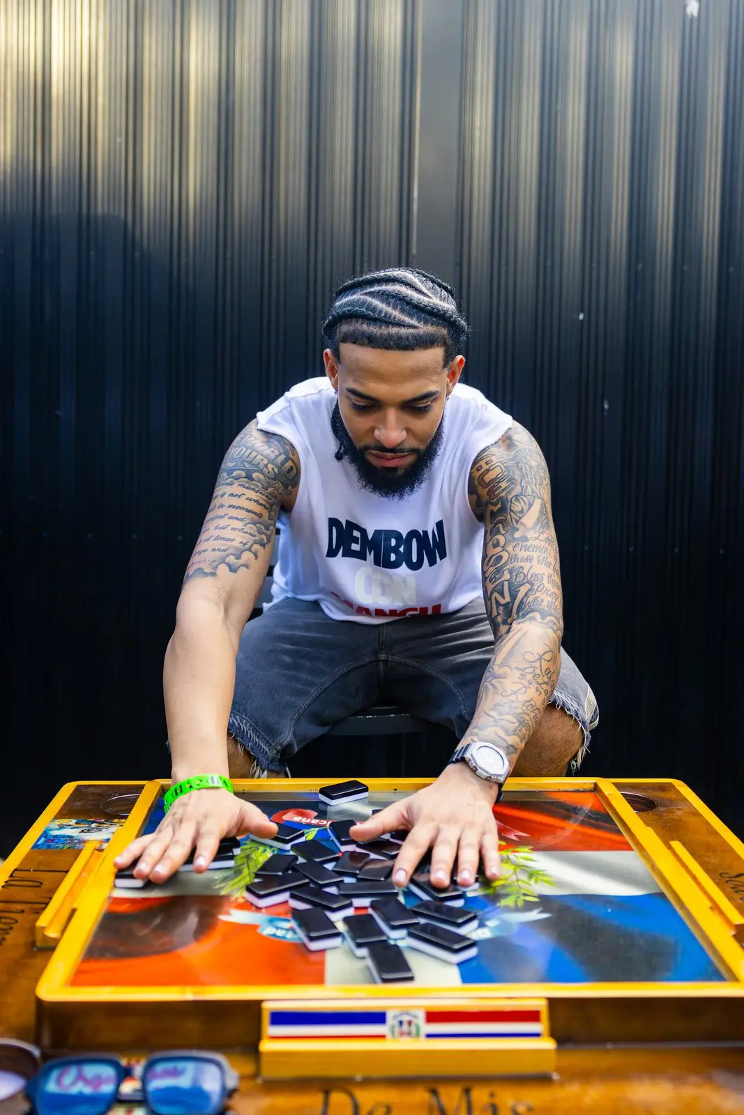A man crouched over a domino table painted with the Dominican flag, laying a tile onto the run.