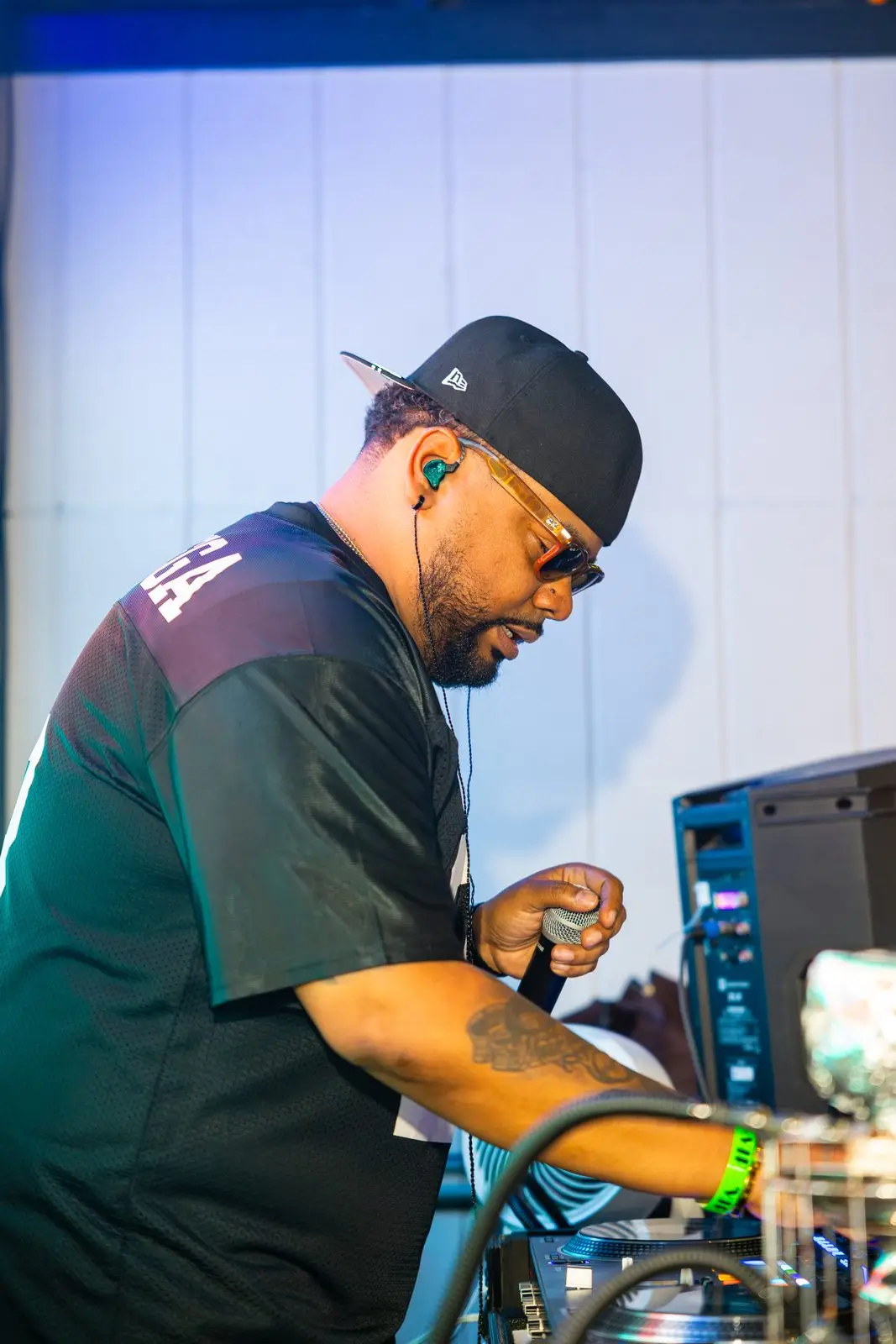 A DJ in a cap and in-ear monitors working the decks in profile, one hand on the mixer.