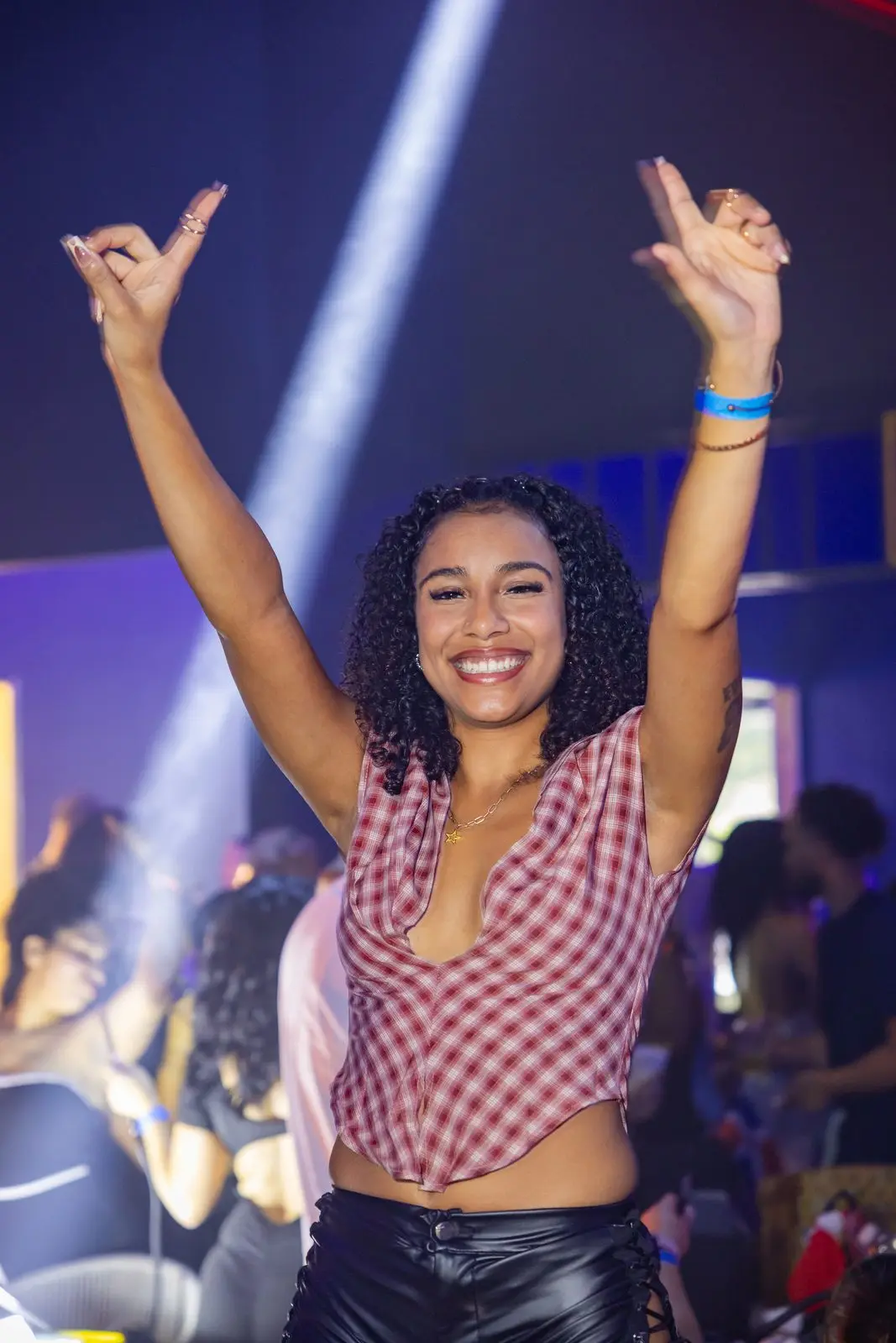A woman laughing with both arms thrown up over her head, a white spotlight beam cutting across the dark room behind her.