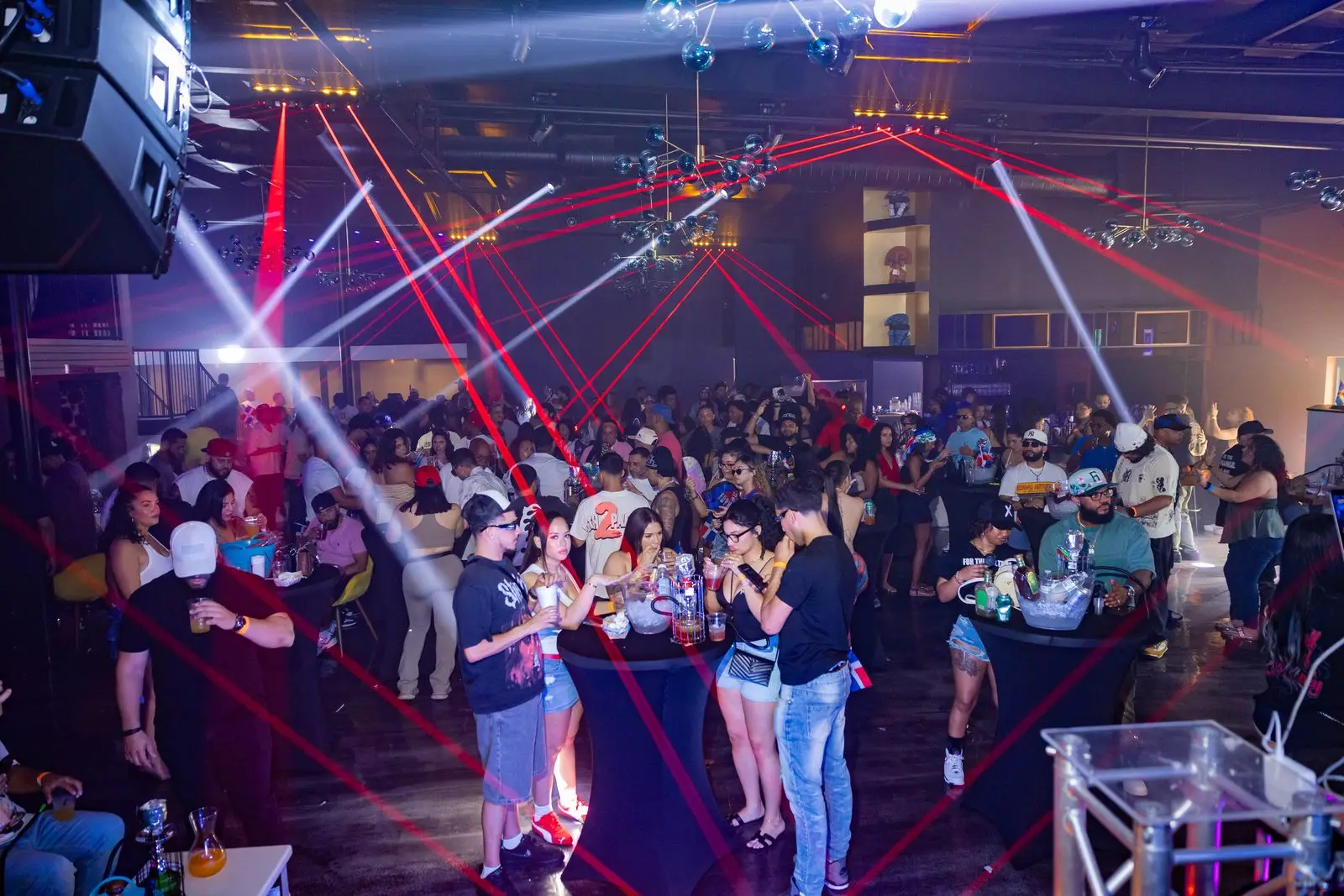A dark room filled wall to wall with people, red laser beams crossing overhead and white spotlights raking the ceiling.