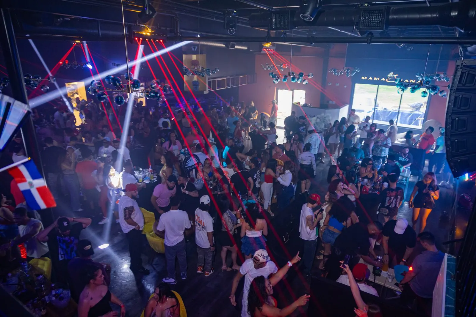 A full floor seen from above, red and white lasers crossing the room, Dominican flags hanging at the left.