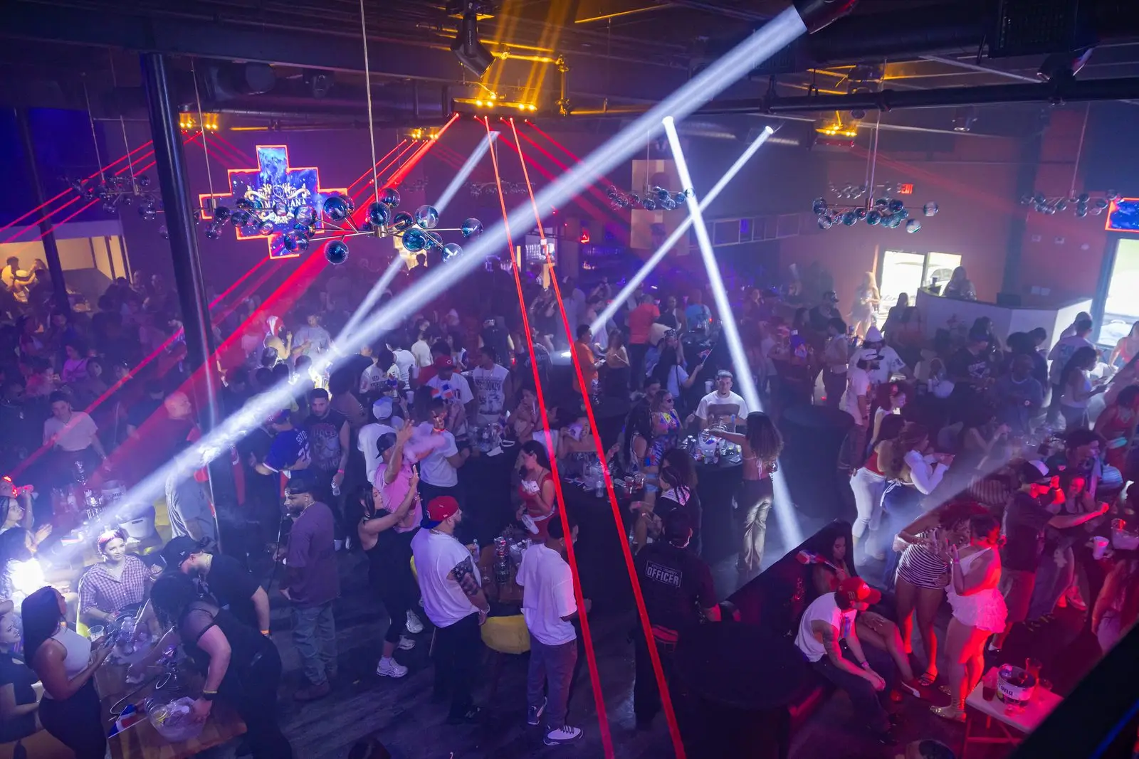 A high view down over a packed floor, white and red beams fanning out across the room above the crowd.